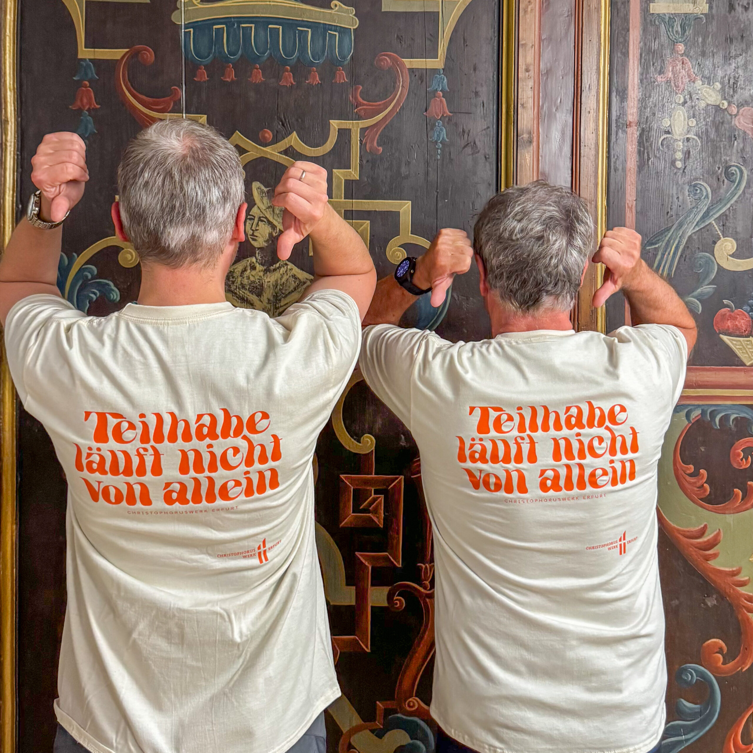 Dr. Björn Starke und Herr Schmidtbauer zeigen den Slogan auf ihren Laufshirts: Teilhabe läuft nicht von allein, in die Kamera.