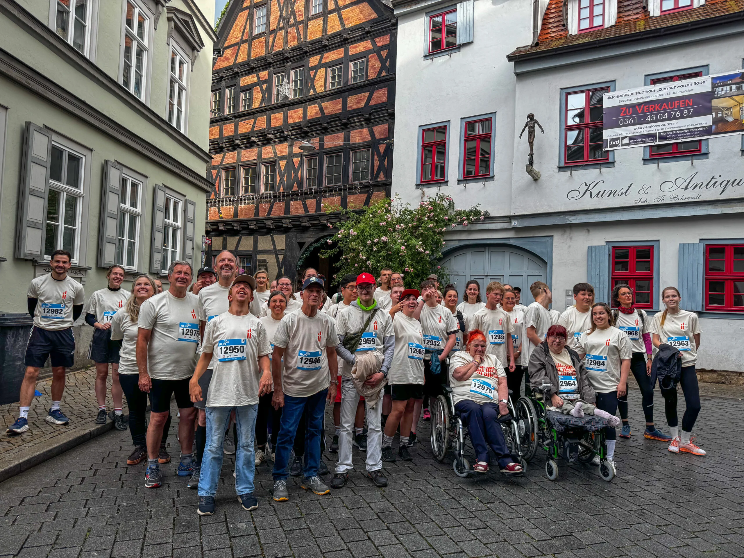Viele Menschen mit und ohne sichbare Behinderung stehen in der Allerheiligenstraße Erfurt und tragen das offizielle RUN-Shirt des Christophoruswerkes. Sie schauen grinsend und euphorisiert in die Kamera.
